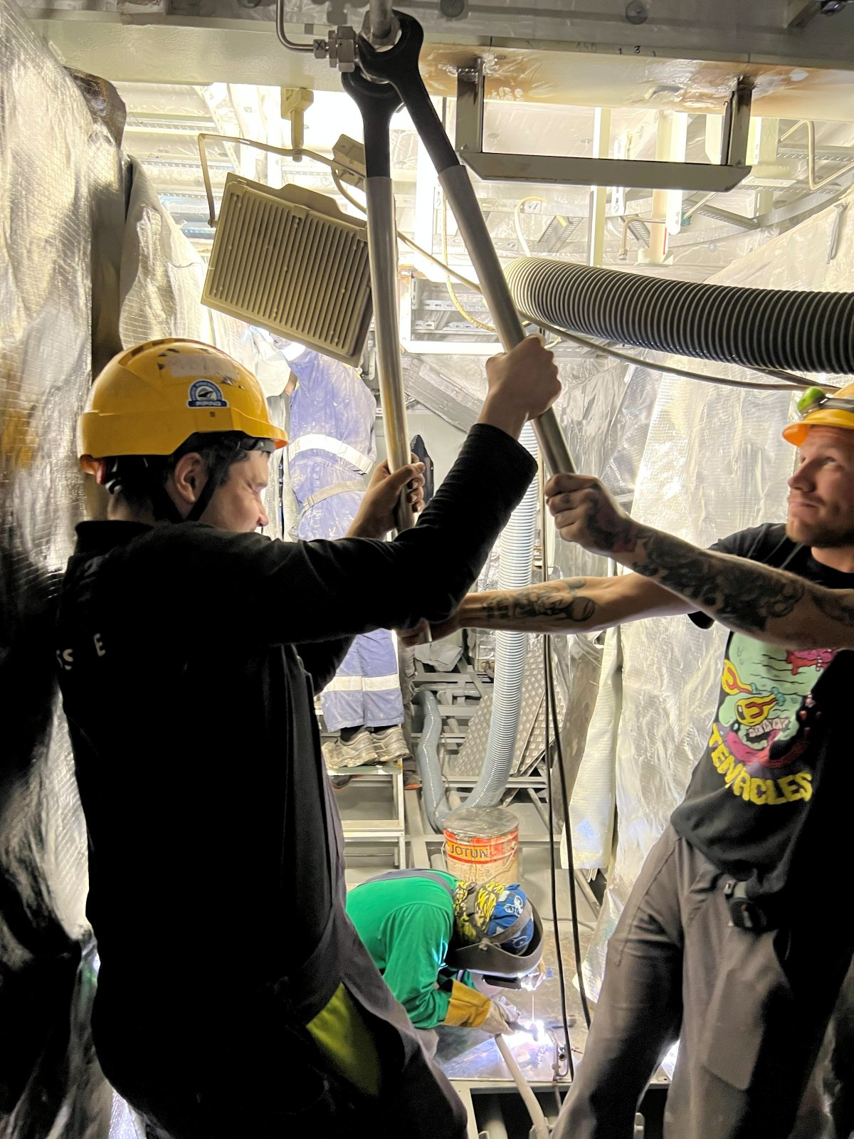 Dwaj monterzy High Pressure Piping prowadzą rurę we dwóch, w tle trzeci spawa